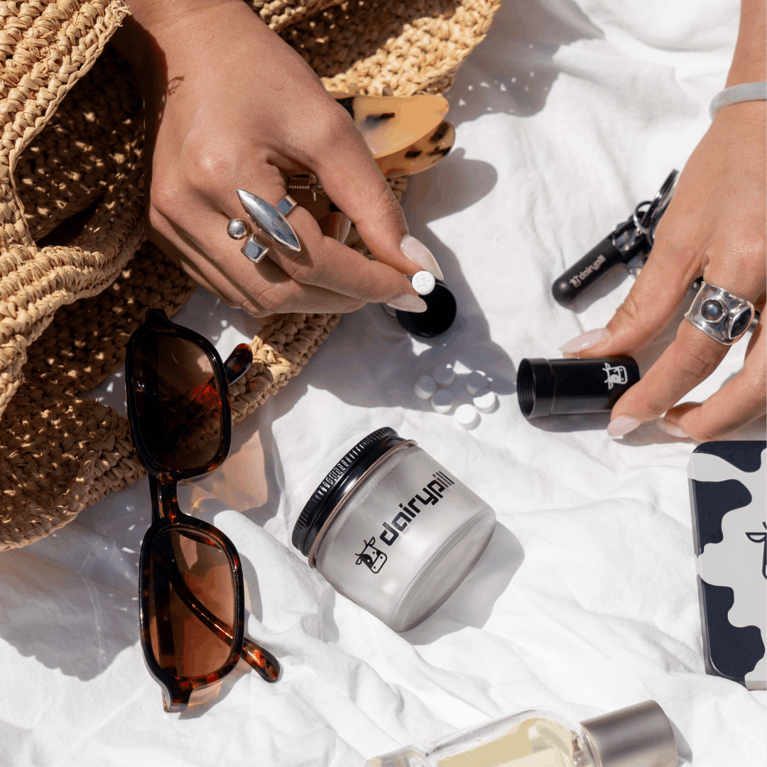 DairyPill Lifestyle Image. Picnic flatlay of glass jar, key pod mini, and key pod max. Model takes DairyPill out of key pod max case.